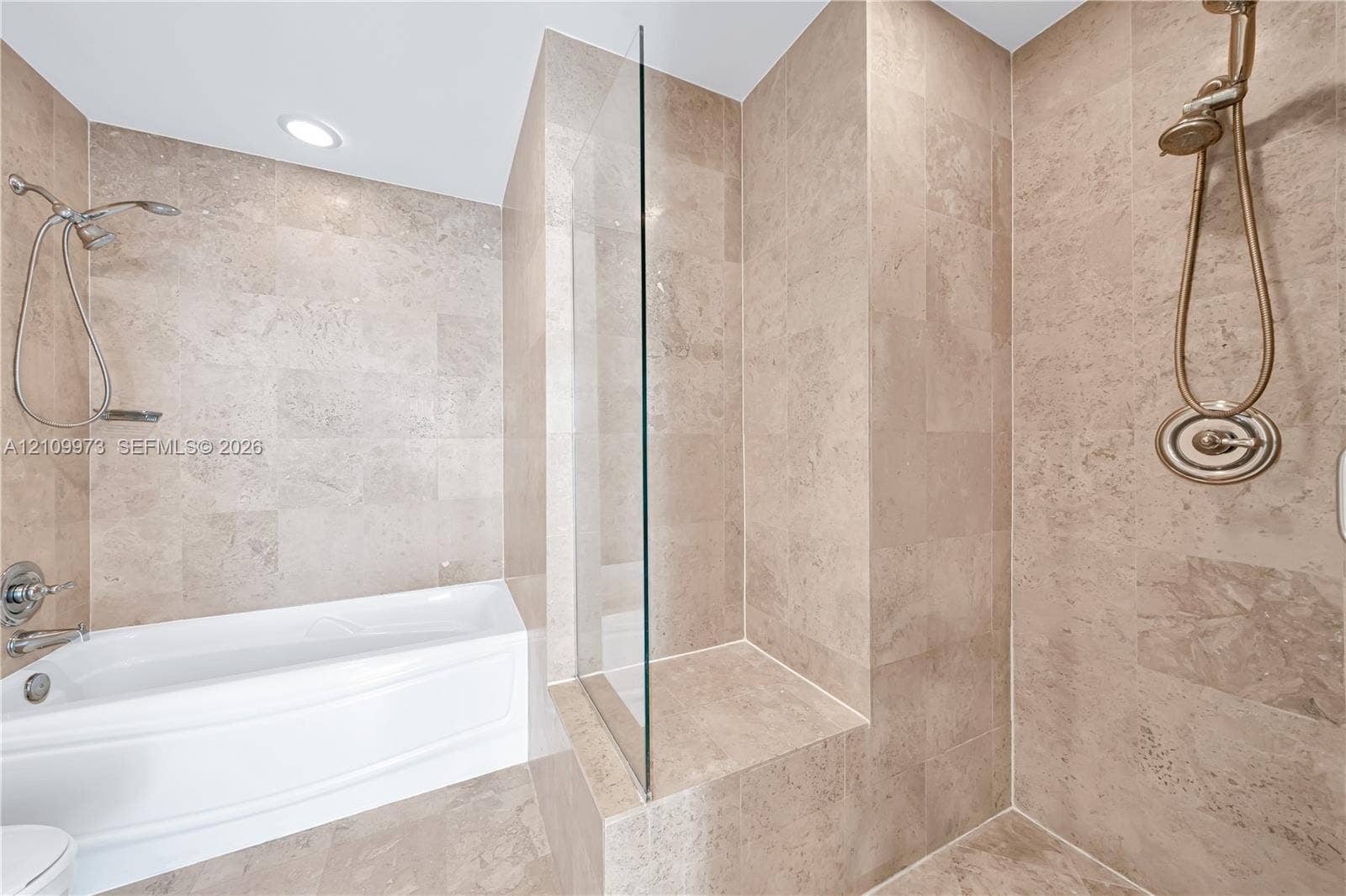 300 S Biscayne Boulevard, #T-1806, Miami, Miami, FL 33131 Soaking tub with a wall-mounted showerhead, separate glass-enclosed shower featuring a built-in tiled bench, and neutral stone-finish tile surround