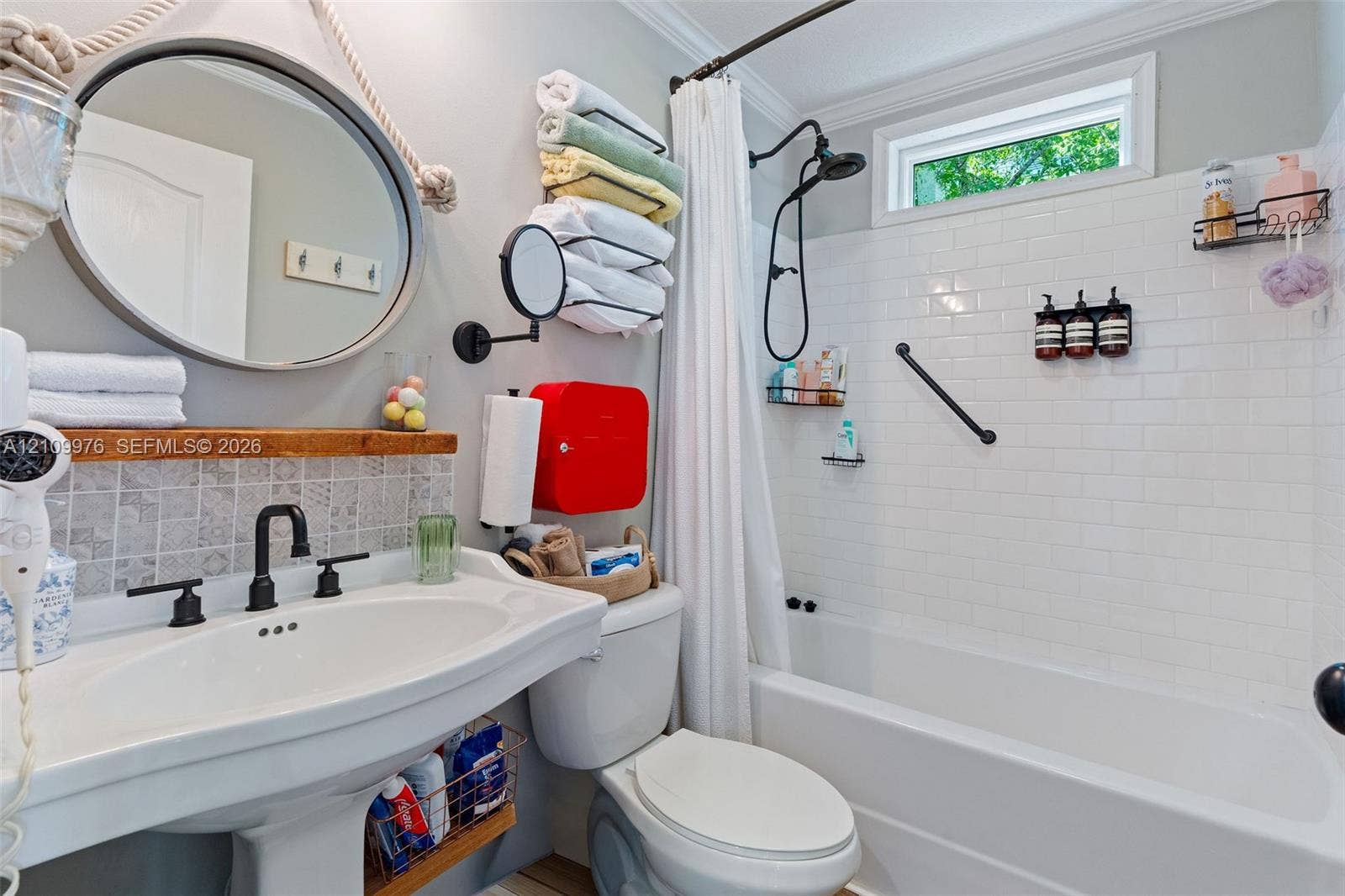 43 Waterways Drive, Key Largo, FL 33037 Bright, updated bathroom featuring a curved pedestal sink with matte black fixtures, subway tile shower surround with glass enclosure, circular mirror with black frame, and white subway tile backsplash above the vanity