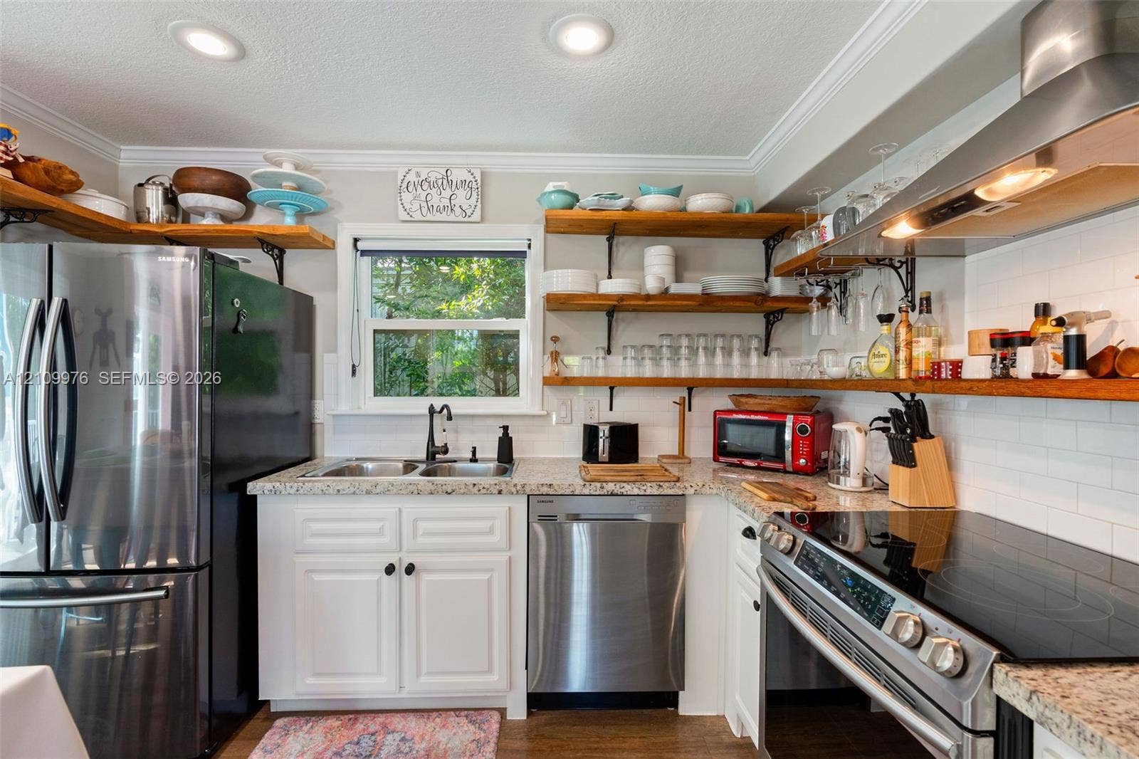 43 Waterways Drive, Key Largo, FL 33037 Kitchen featuring stainless steel appliances, speckled stone countertops, white cabinetry, open wood shelving, and a glass-tiled backsplash