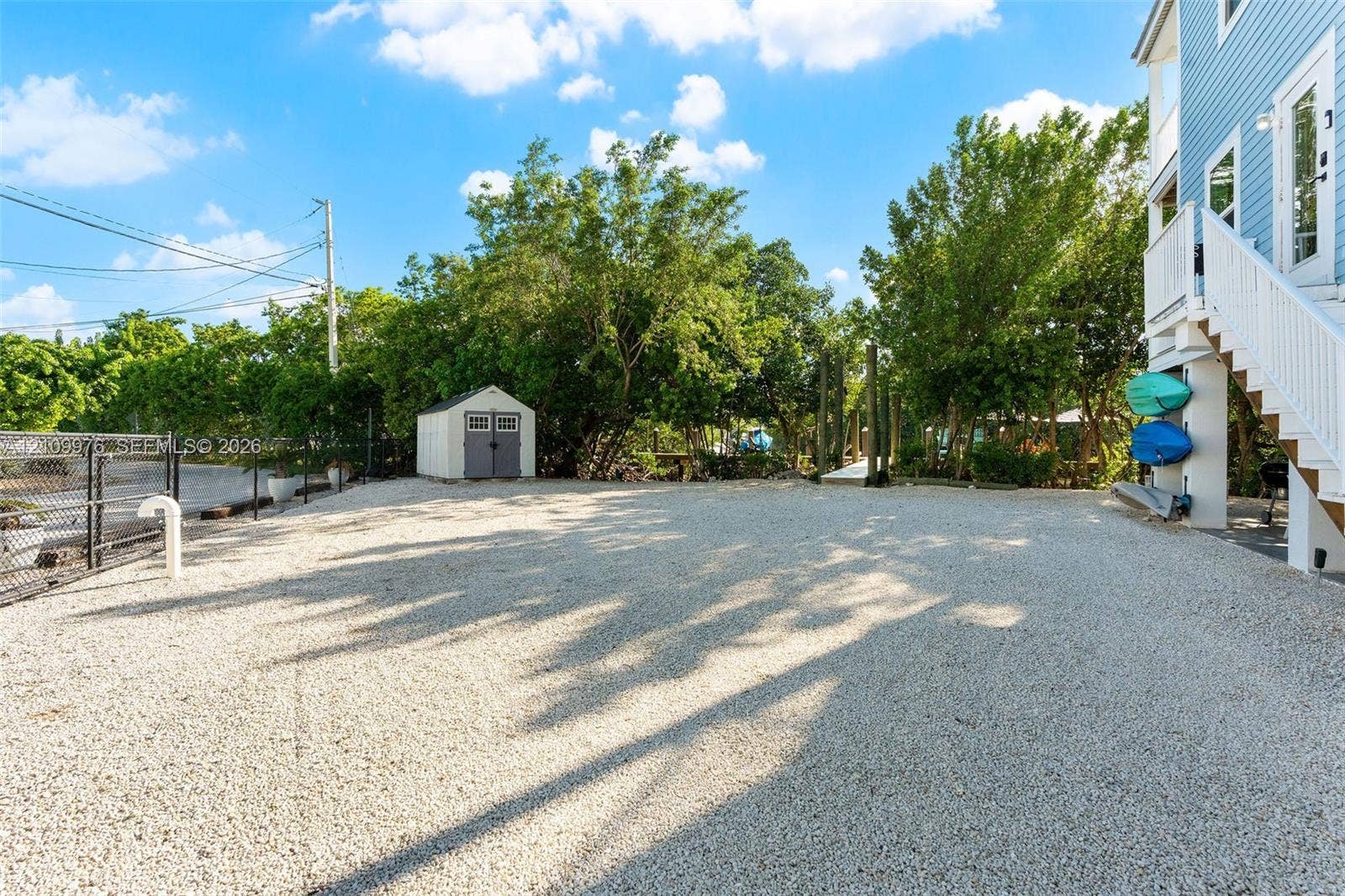 43 Waterways Drive, Key Largo, FL 33037 Gravel-surfaced exterior lot featuring a detached storage shed, perimeter chain-link fencing, and elevated home foundation