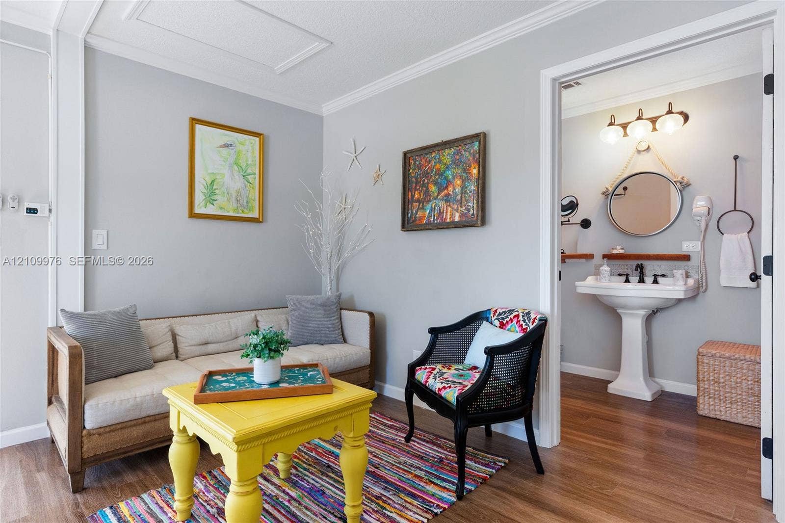 43 Waterways Drive, Key Largo, FL 33037 Interior space featuring wood-finish flooring and crown molding, with an opening to a bathroom equipped with a pedestal sink, three-bulb vanity lighting, and a circular mirror suspended by rope