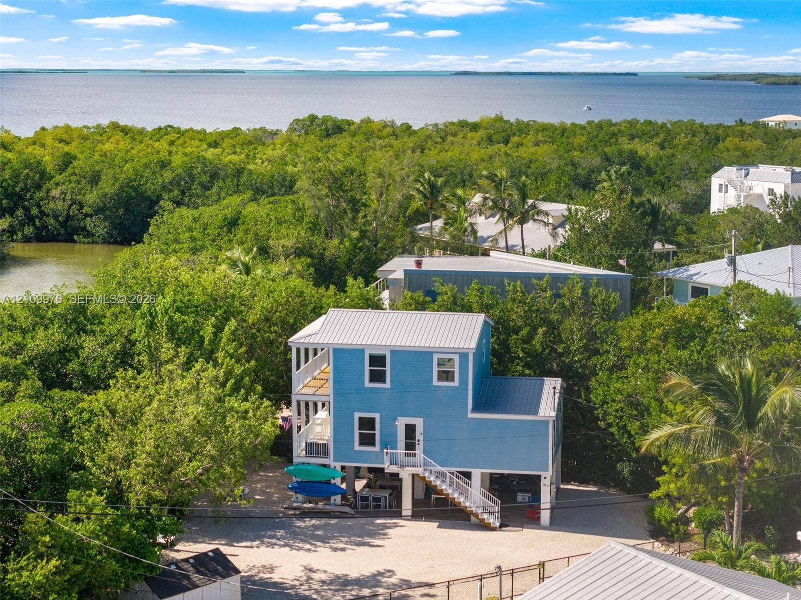 43 Waterways Drive, Key Largo, FL 33037 Elevated two-story residence with horizontal siding, metal roofing, dual-level covered porches, and an exterior metal staircase