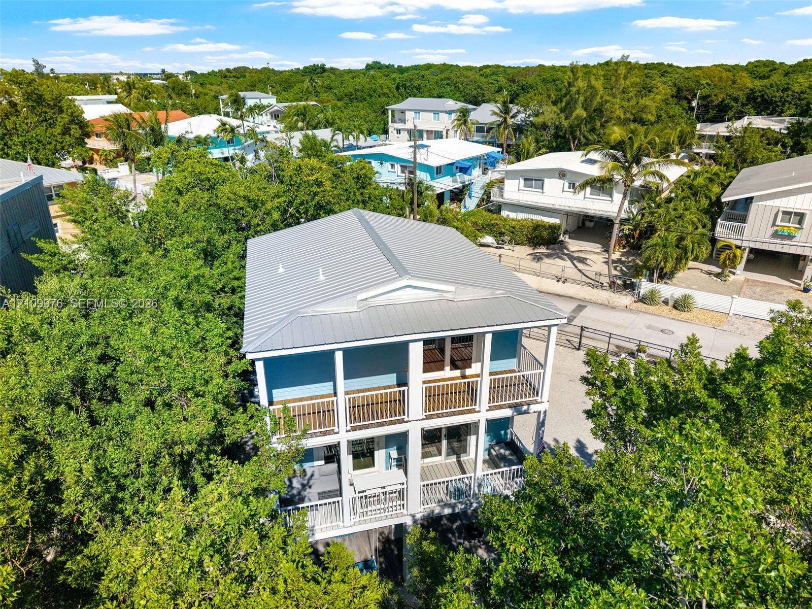 43 Waterways Drive, Key Largo, FL 33037 Two-story property featuring a metal roof, stacked exterior balconies with white railings, and a gravel driveway