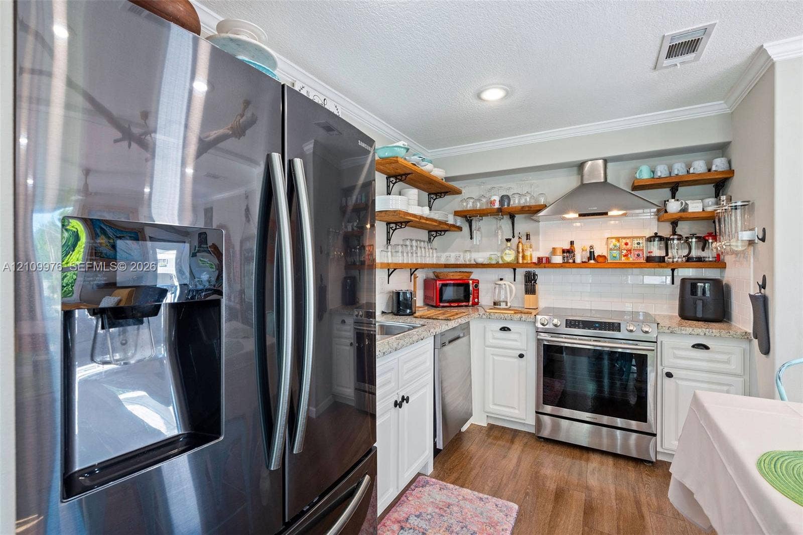 43 Waterways Drive, Key Largo, FL 33037 Kitchen featuring stainless steel appliances, stone-look countertops, white cabinetry with crown molding, natural wood-finish open shelving, and a white subway tile backsplash