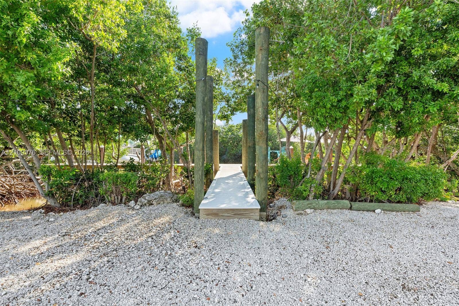 43 Waterways Drive, Key Largo, FL 33037 Waterfront dock featuring pilings, light-colored decking, and natural shell shoreline bordered by mature trees and native vegetation
