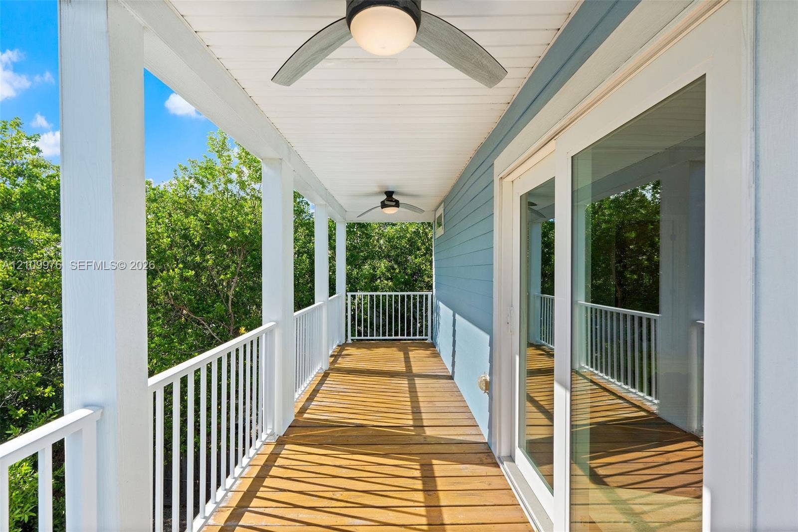 43 Waterways Drive, Key Largo, FL 33037 Covered balcony featuring wood-plank flooring, white metal railing, dual ceiling fans with integrated lighting, and horizontal lap siding