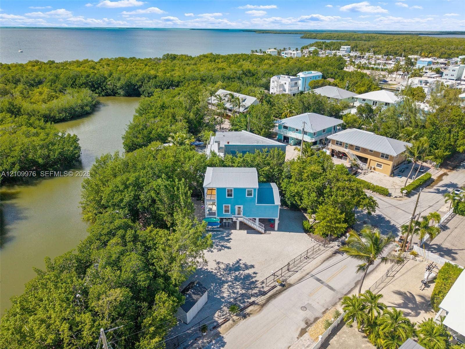 43 Waterways Drive, Key Largo, FL 33037 Elevated residence featuring a metal roof, light-toned gravel lot, and waterfront positioning along a natural canal