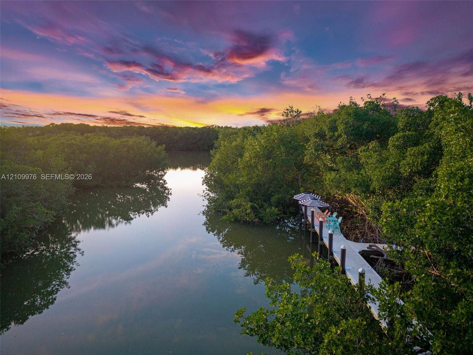 43 Waterways Drive, Key Largo, FL 33037 Waterfront property featuring a private dock and mature mangrove surroundings under a prominent sunset backdrop