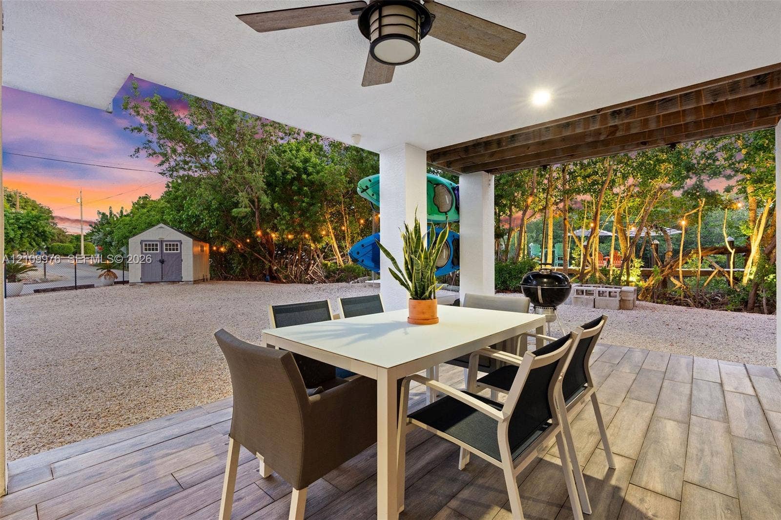 43 Waterways Drive, Key Largo, FL 33037 Covered patio featuring wood-finish tile flooring, ceiling fan, and exposed wood-beam detailing, opening to a gravel courtyard with a storage structure
