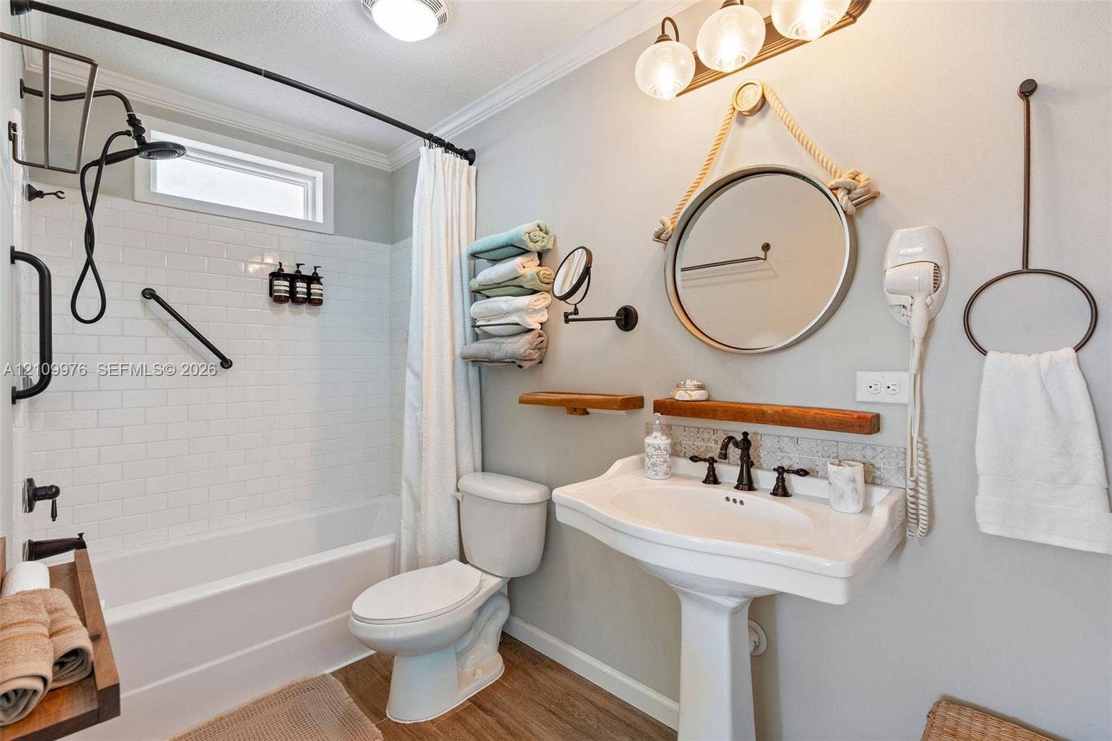 43 Waterways Drive, Key Largo, FL 33037 Bathroom featuring white subway tile tub surround, pedestal sink with multi-handle oil-rubbed bronze faucet, round wall-mounted mirror, wood-finish flooring, and industrial-style multi-light fixture