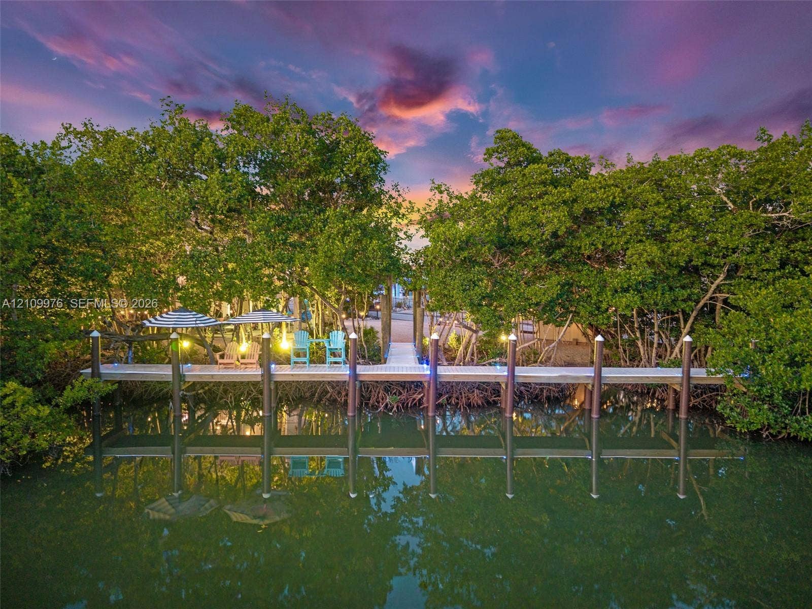 43 Waterways Drive, Key Largo, FL 33037 Waterfront wooden dock featuring structural pilings, integrated string lighting, and direct access to mature mangrove vegetation