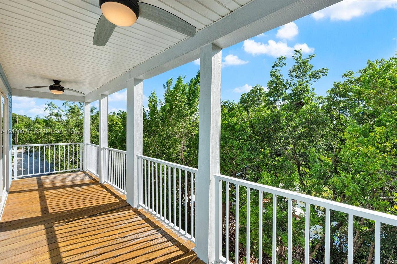 43 Waterways Drive, Key Largo, FL 33037 Covered balcony featuring wood decking, white baluster railings, dual ceiling fans with integrated lighting, and a white beadboard ceiling