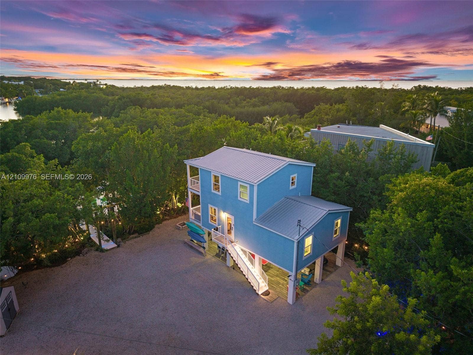 43 Waterways Drive, Key Largo, FL 33037 Elevated multi-level residence featuring a metal roof, wraparound balconies, exterior staircase, and a sprawling gravel grounds area