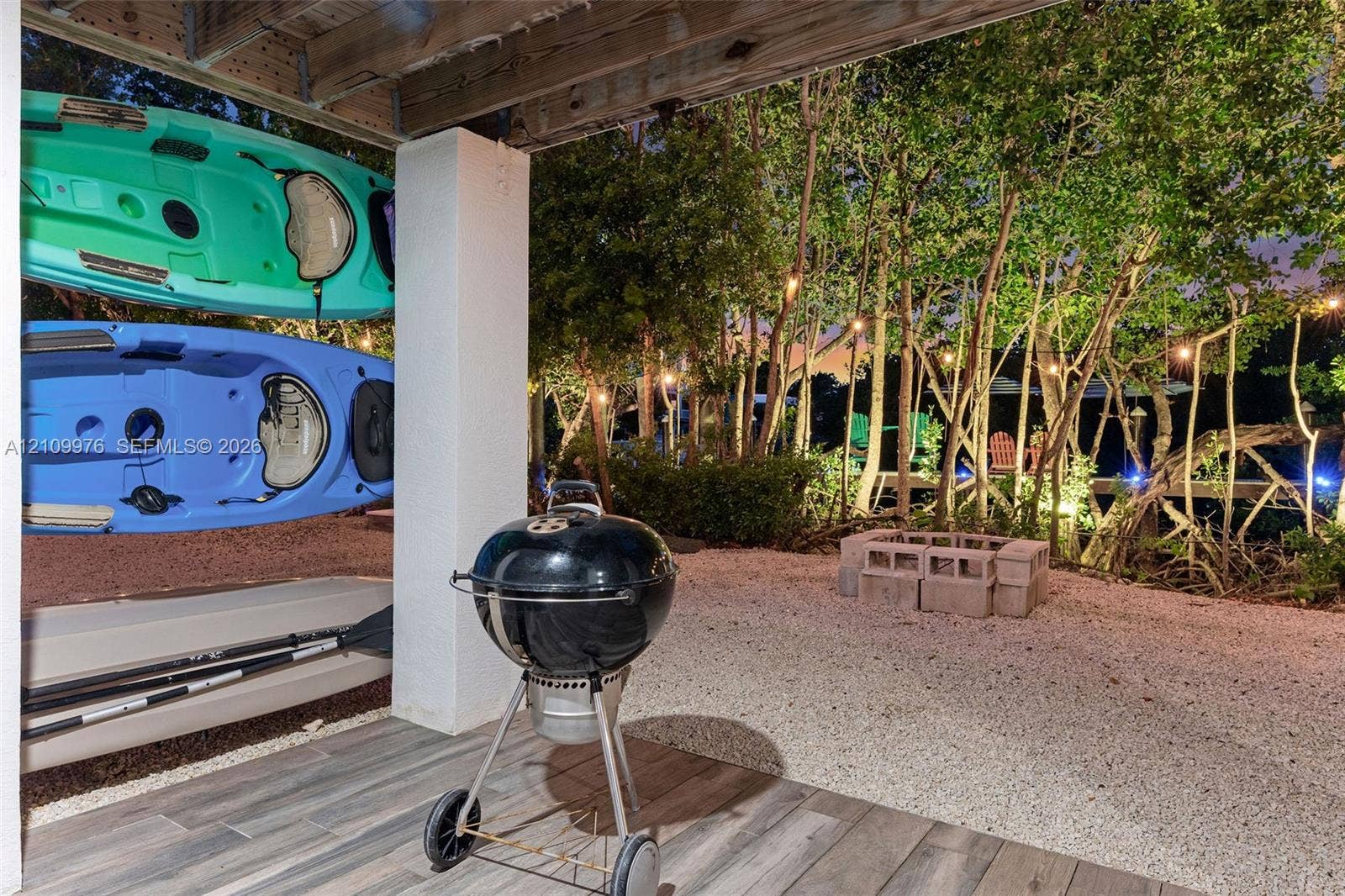 43 Waterways Drive, Key Largo, FL 33037 Covered patio with wood-finish tile flooring, crushed stone ground cover, masonry block fire pit, and mature perimeter trees