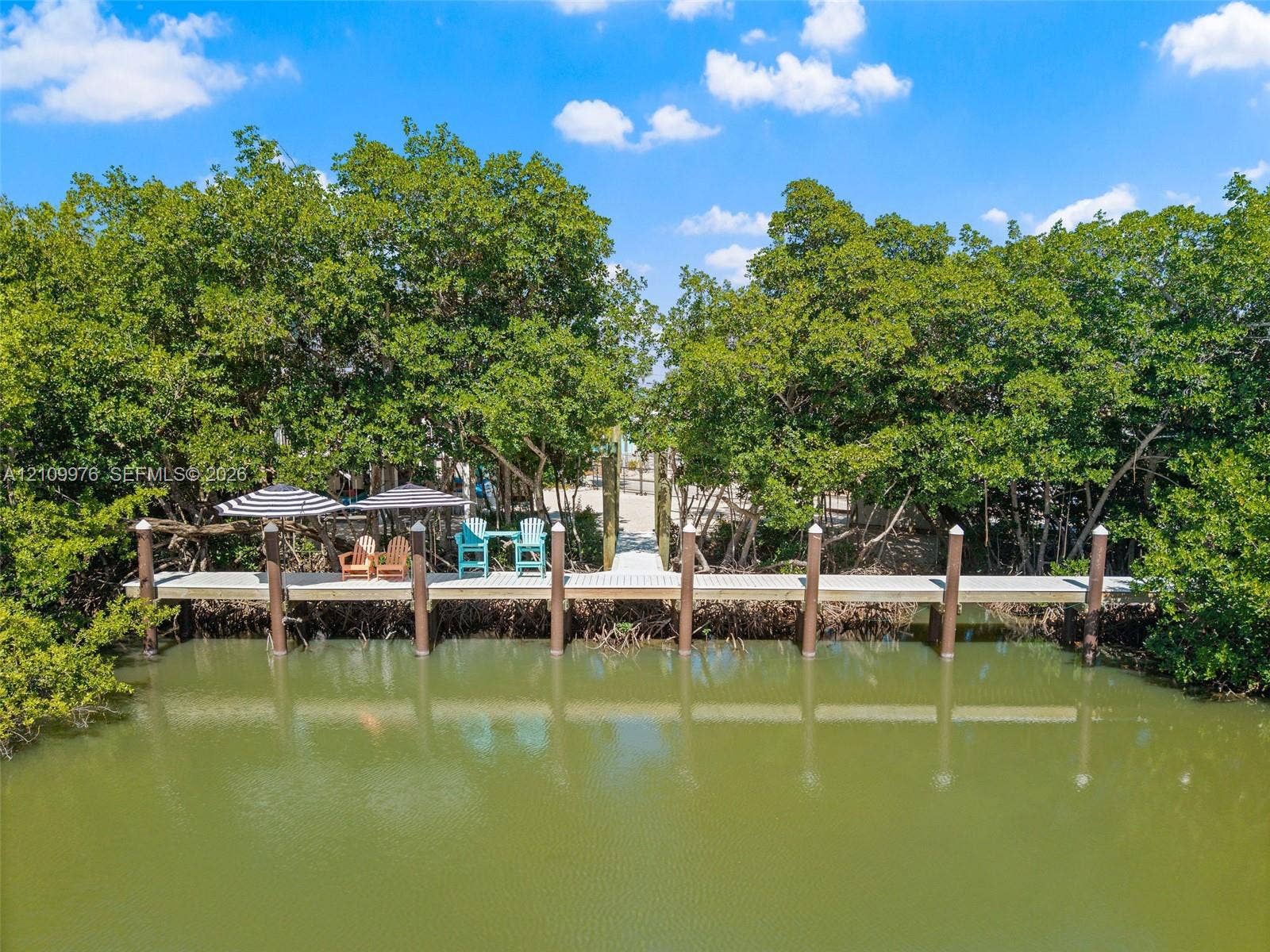 43 Waterways Drive, Key Largo, FL 33037 Private dock featuring wood-plank decking and anchored pilings, surrounded by mature trees