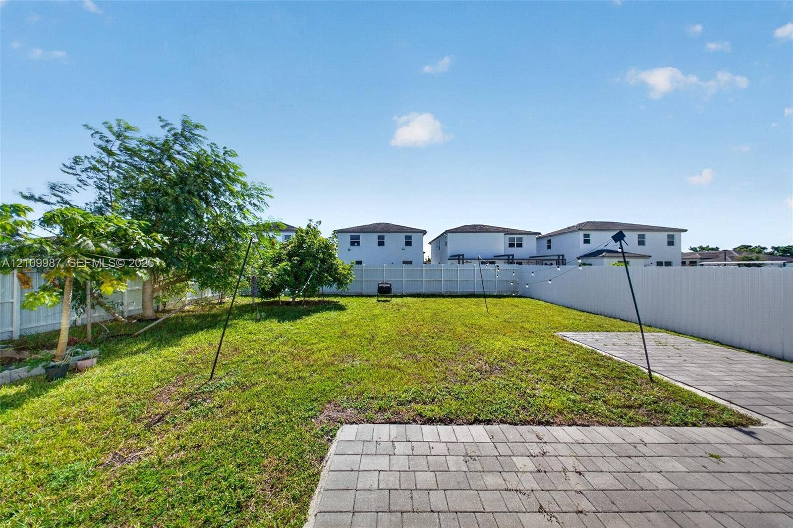 Fenced backyard featuring a manicured lawn, paver patio, and mature trees