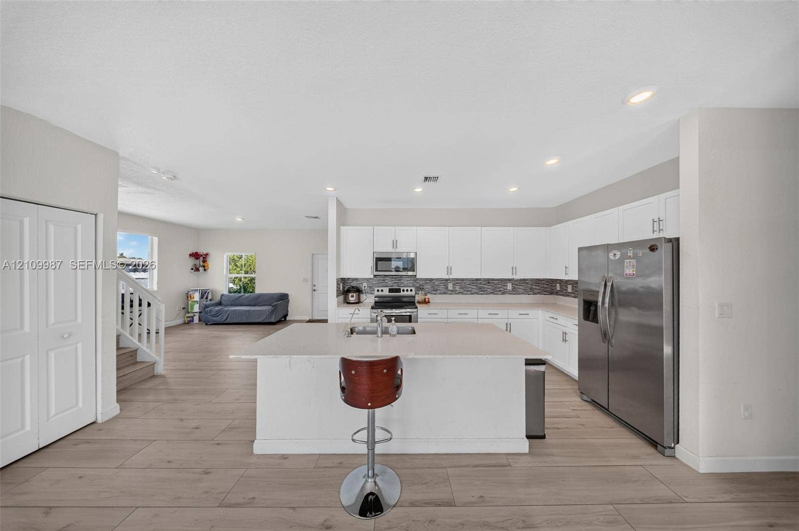 Kitchen featuring white shaker-style cabinetry, quartz countertops, a central island with an integrated sink, stainless steel appliances, and porcelain flooring