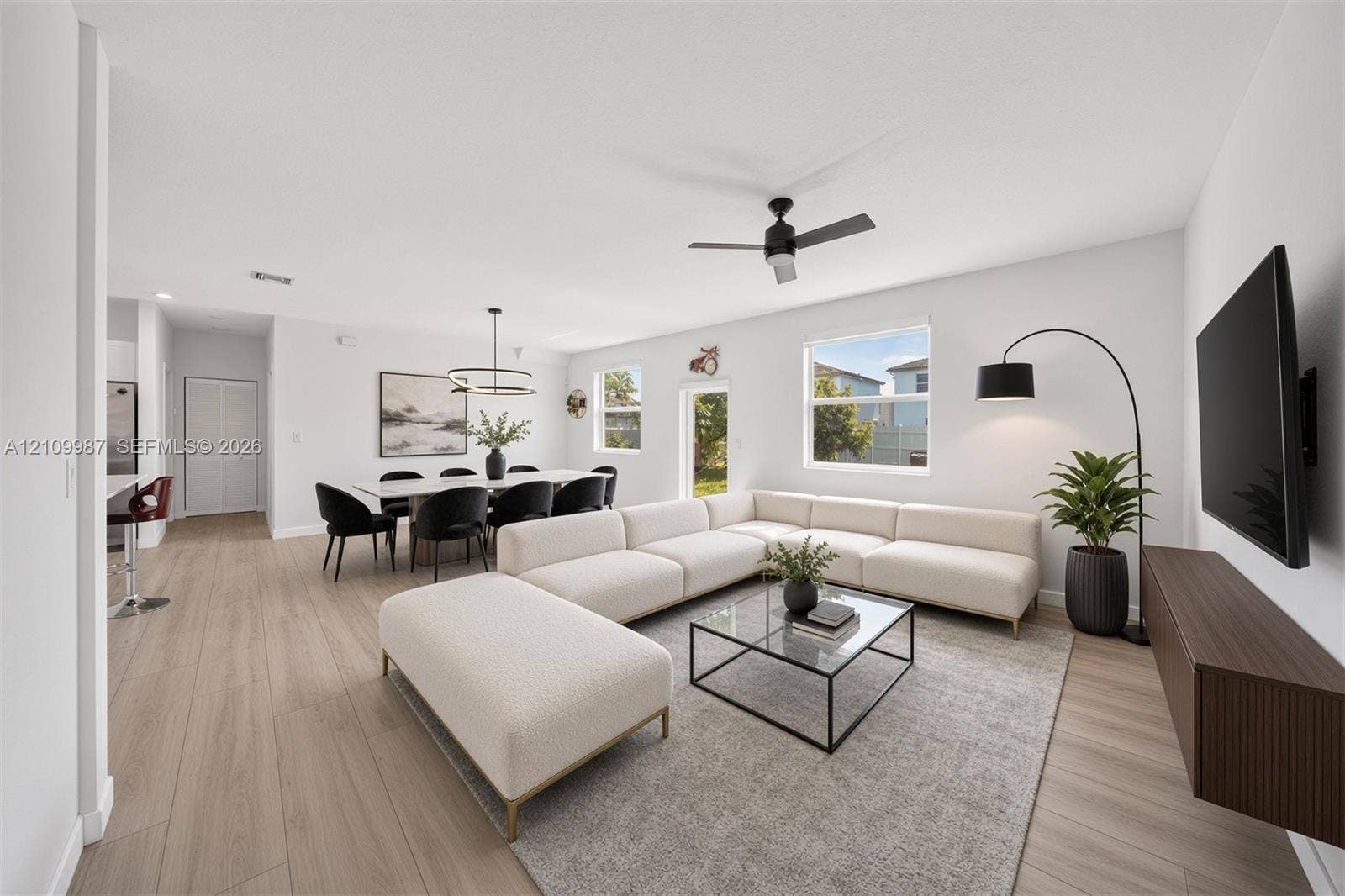 Staged Open-concept interior featuring porcelain flooring, ceiling fan with integrated lighting, dual-tiered modern chandelier, and a wall-mounted floating cabinetry unit