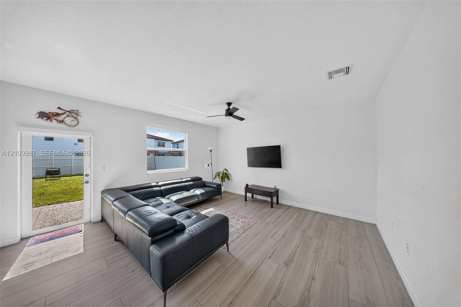 Living area featuring neutral-toned wood-finish flooring, a ceiling fan, and a glass-paneled exterior door