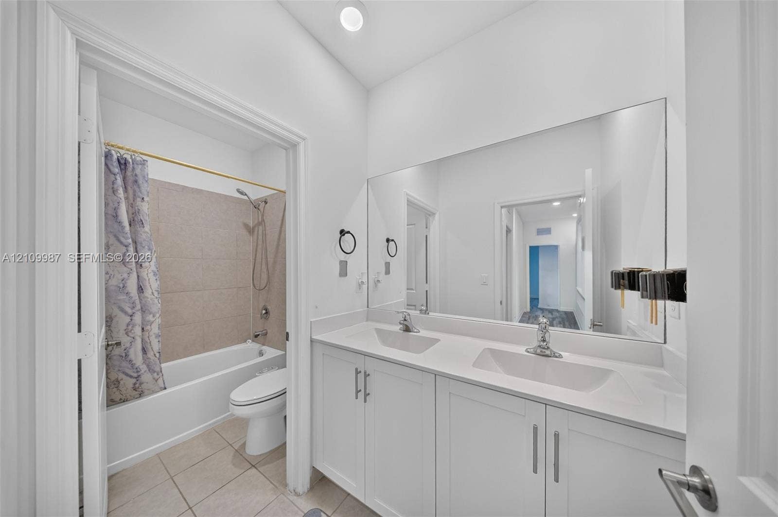 Dual-sink vanity with a solid-surface countertop, full-width wall mirror, and tub-shower combination featuring tile surround