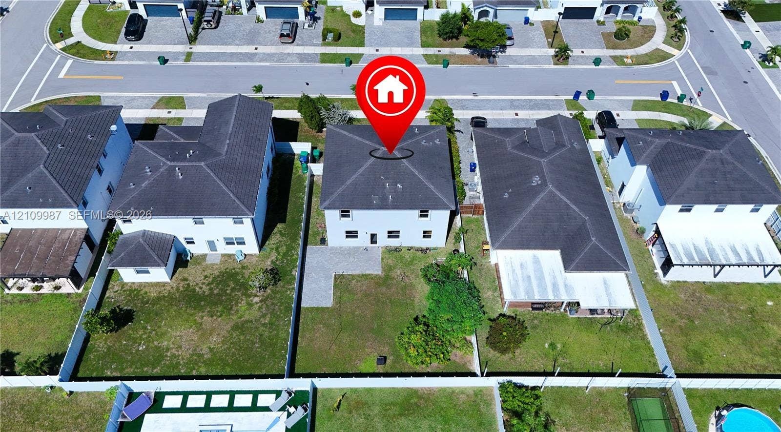 12740 SW 214th Terrace, Miami, FL 33177 Two-story residential property featuring a hipped roof, light-toned exterior finish, a stone-paved patio area, and a fully fenced backyard