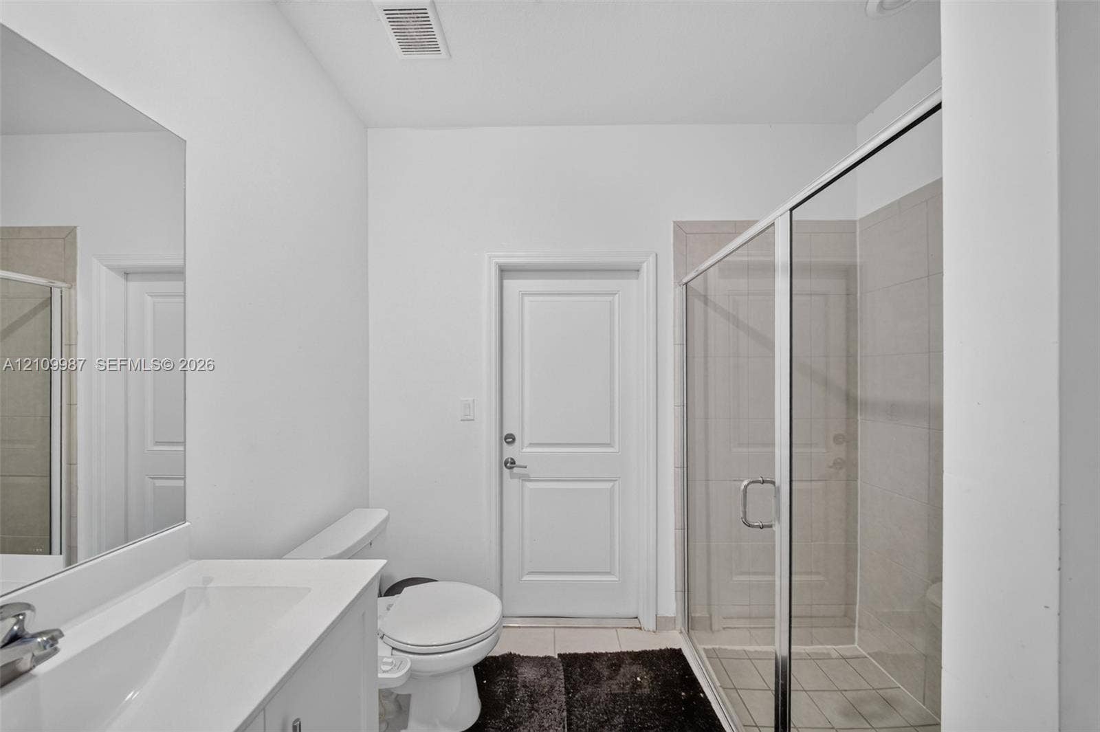Bathroom featuring a vanity with a white countertop and integrated sink, a glass-enclosed shower with tile surround, and a wall-mounted mirror