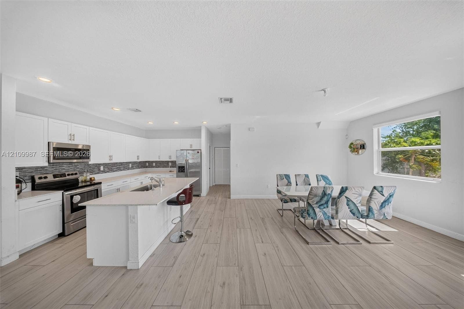 Open-concept kitchen featuring white shaker-style cabinetry, stainless steel appliances, a central island with a quartz countertop