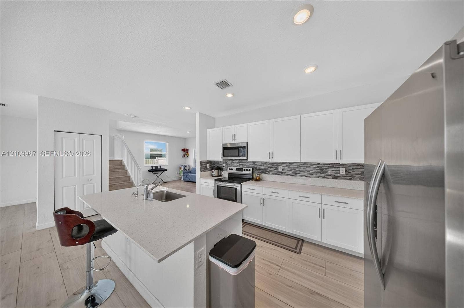 Kitchen featuring white cabinetry, stone-finish countertops, stainless steel appliances, a center island with an integrated sink, and wood-finish flooring