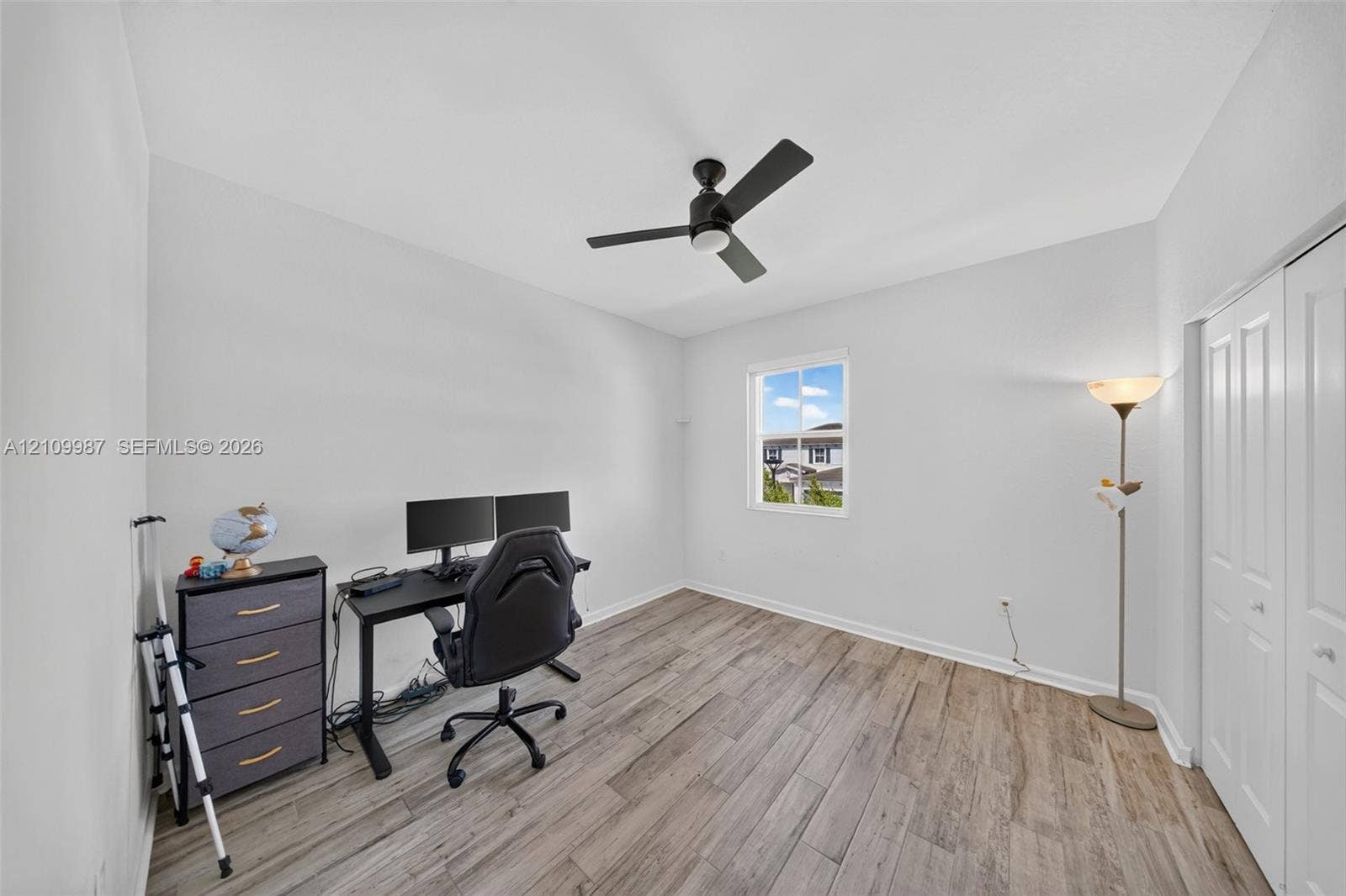 Neutral-toned room featuring porcelain flooring, a matte black ceiling fan with integrated light, and dual-panel closet doors