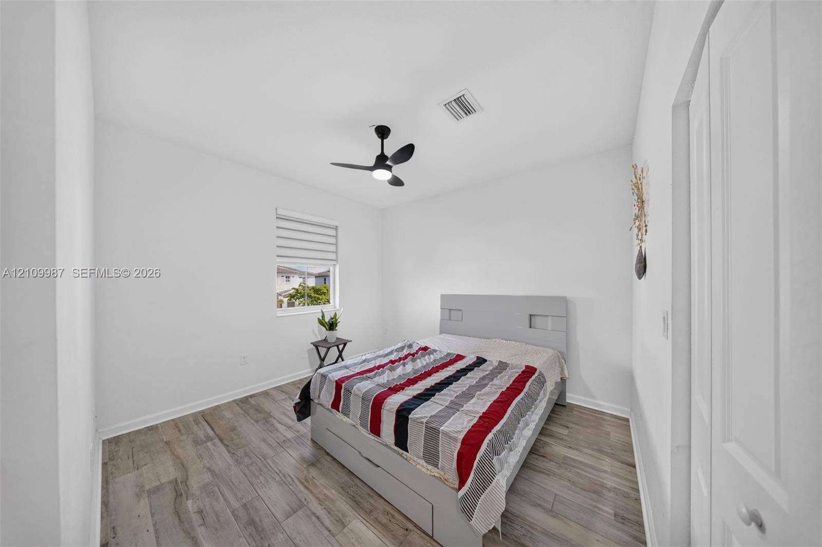 Bedroom featuring porcelain flooring, a matte black ceiling fan with integrated lighting, and a window with adjustable roller shades