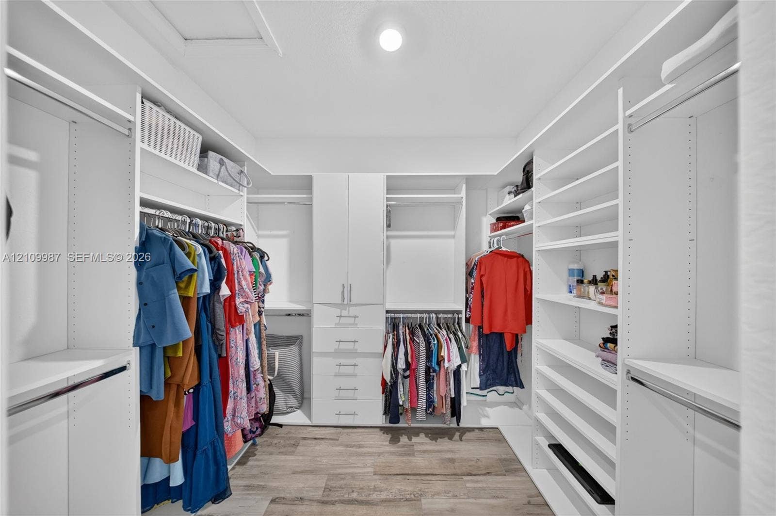 Walk-in closet featuring white custom built-in shelving, a dedicated drawer stack with brushed metal hardware, and porcelain flooring