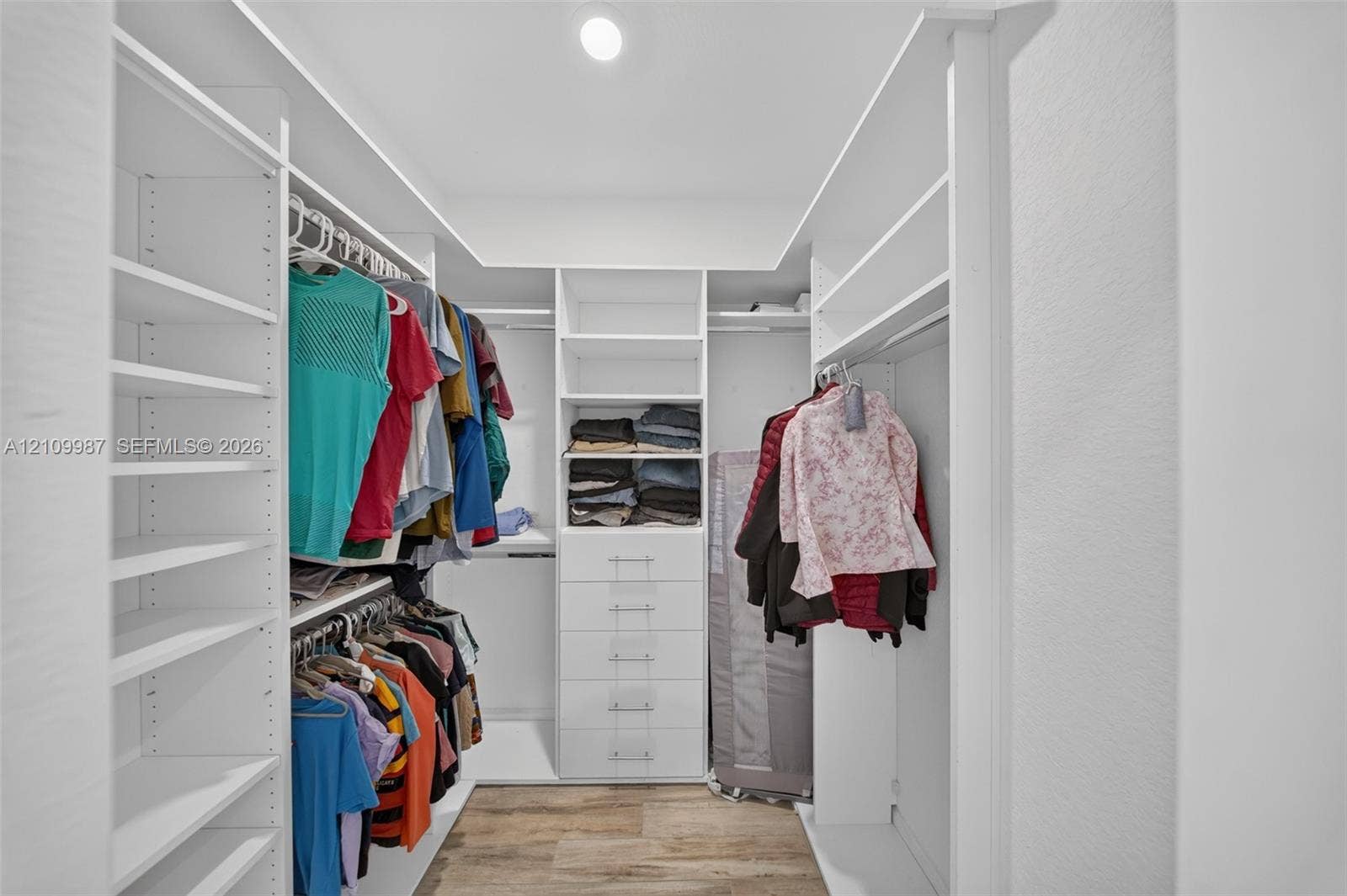 Walk-in closet featuring white custom built-in shelving, a dedicated drawer stack, overhead lighting, and porcelain flooring