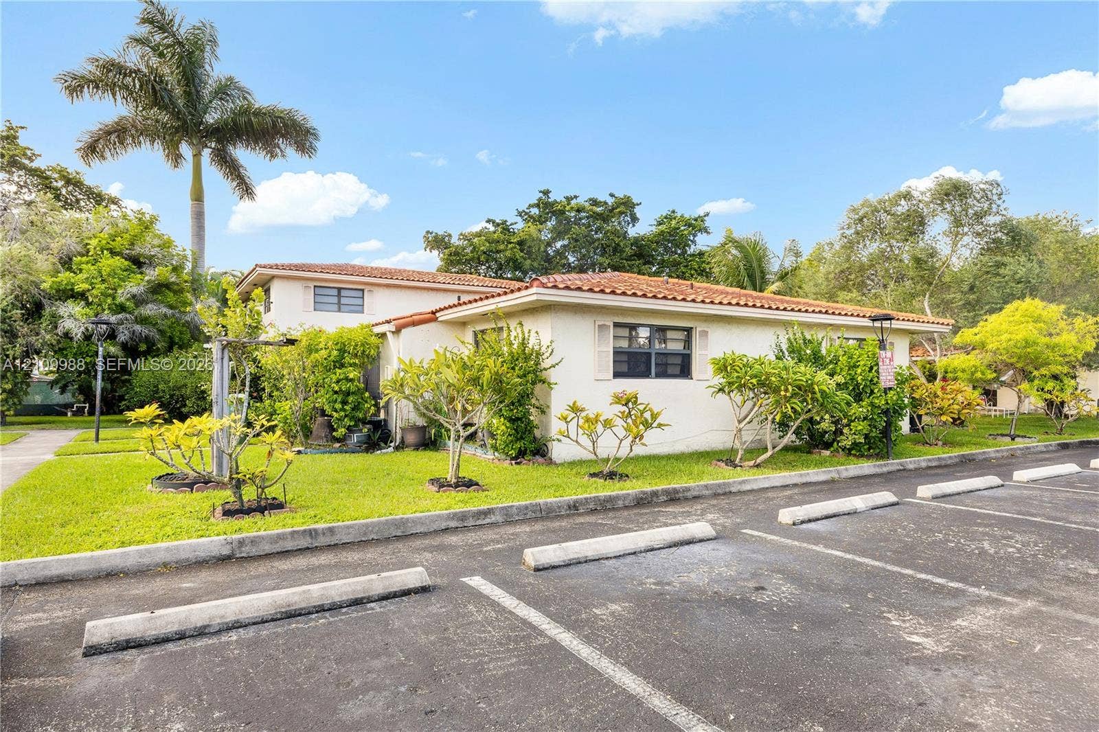 13946 NE 4th Avenue, #13946, Miami, FL 33161 Stucco exterior featuring a terracotta tile roof, designated asphalt parking spaces, and established landscaping with mature palm trees