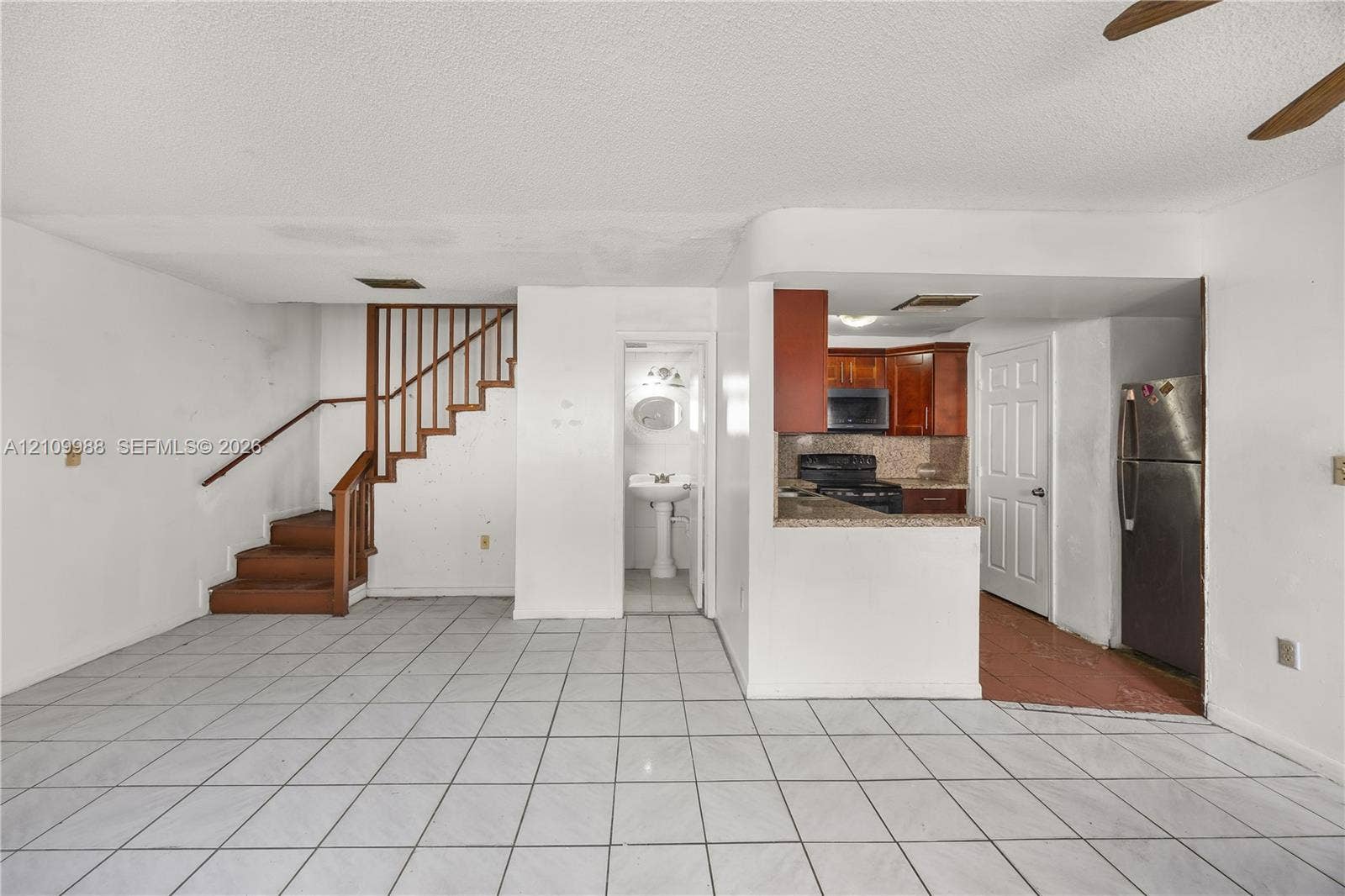 13946 NE 4th Avenue, #13946, Miami, FL 33161 Interior featuring white tile flooring, wooden staircase with matching handrail, kitchen with dark wood cabinetry and stone countertops, and a pedestal sink