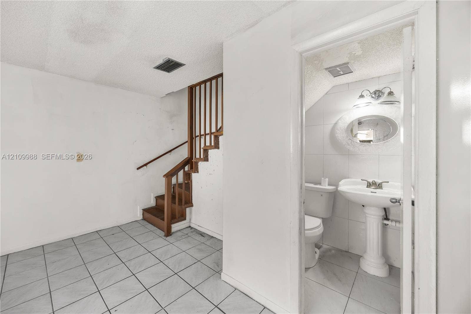 13946 NE 4th Avenue, #13946, Miami, FL 33161 Staircase with wood railings and matching treads, tile flooring, pedestal sink, wall-mounted mirror, and wall-mounted light fixture