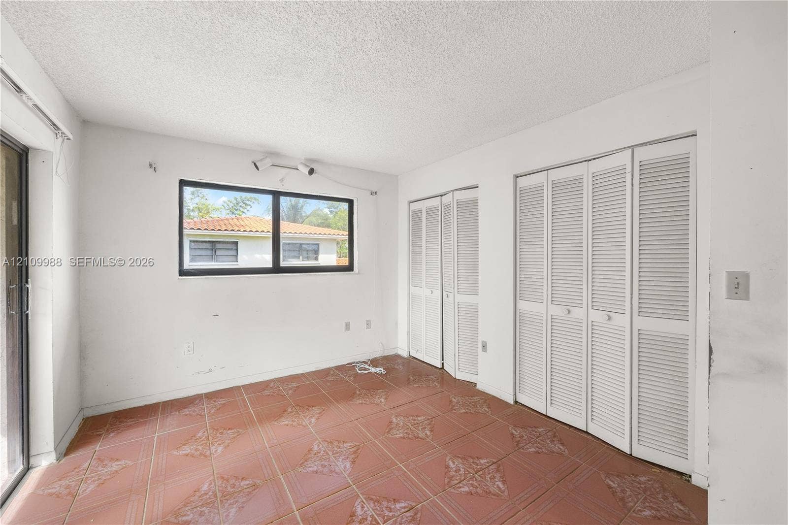 13946 NE 4th Avenue, #13946, Miami, FL 33161 Room featuring terracotta-style tile flooring, dual sets of white louvered-door closets, and a large window with black frames