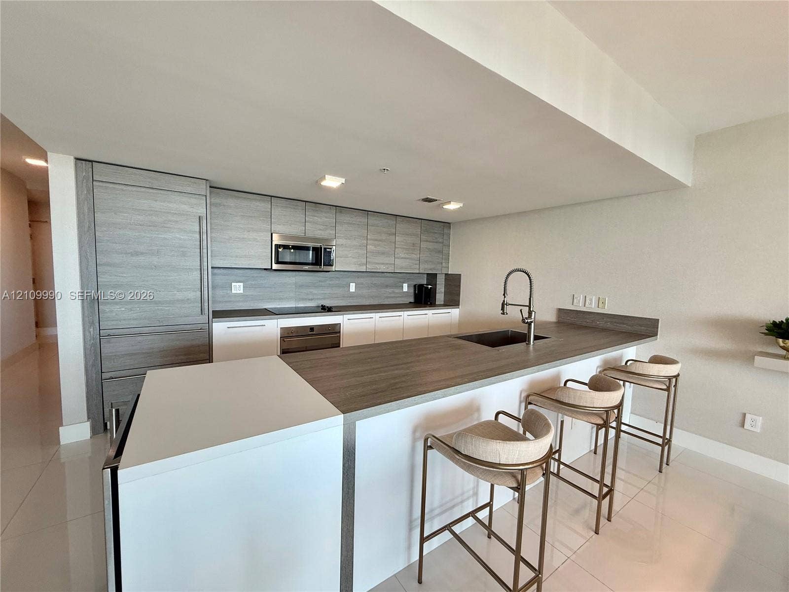 Kitchen featuring wood-finish cabinetry, integrated appliances, a central island with an extended breakfast bar, and a gooseneck faucet