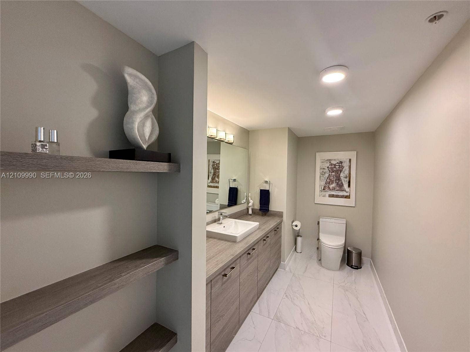 Built-in wood-finish shelving, vanity with integrated cabinetry, vessel sink, polished surface countertop, and large-format tile flooring