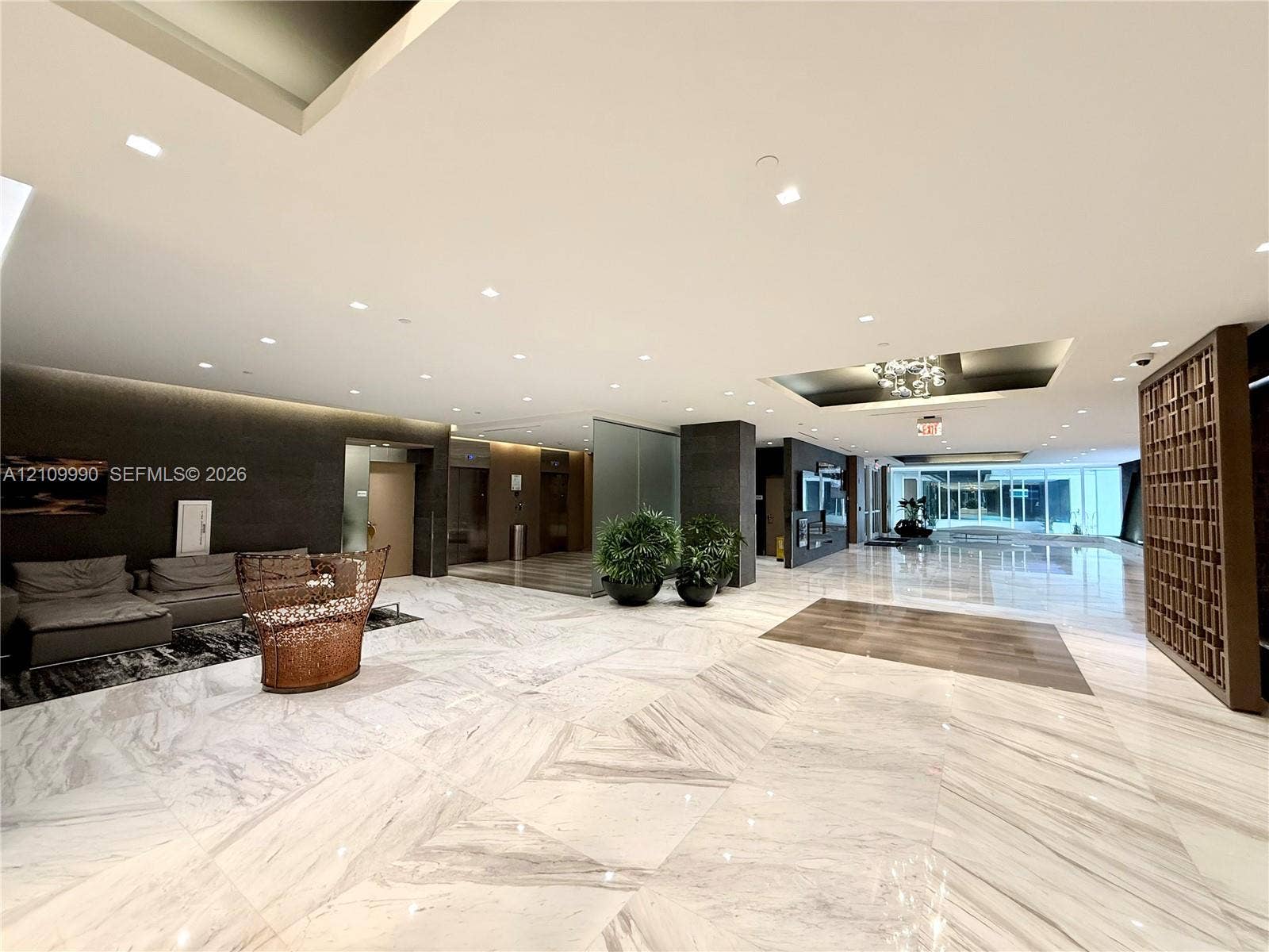 Expansive lobby featuring large-format stone tile flooring, recessed ceiling lighting, a decorative geometric wood screen, and high-gloss finishes
