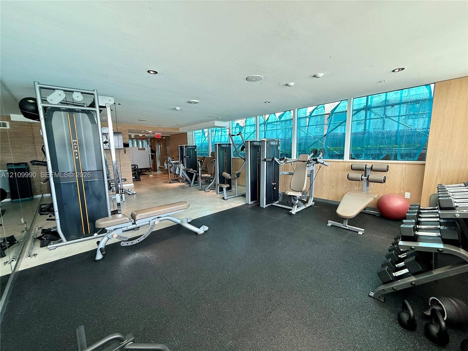Fitness center featuring expansive floor-to-ceiling windows, rubberized athletic flooring, recessed ceiling lighting, and wood-finish wall paneling