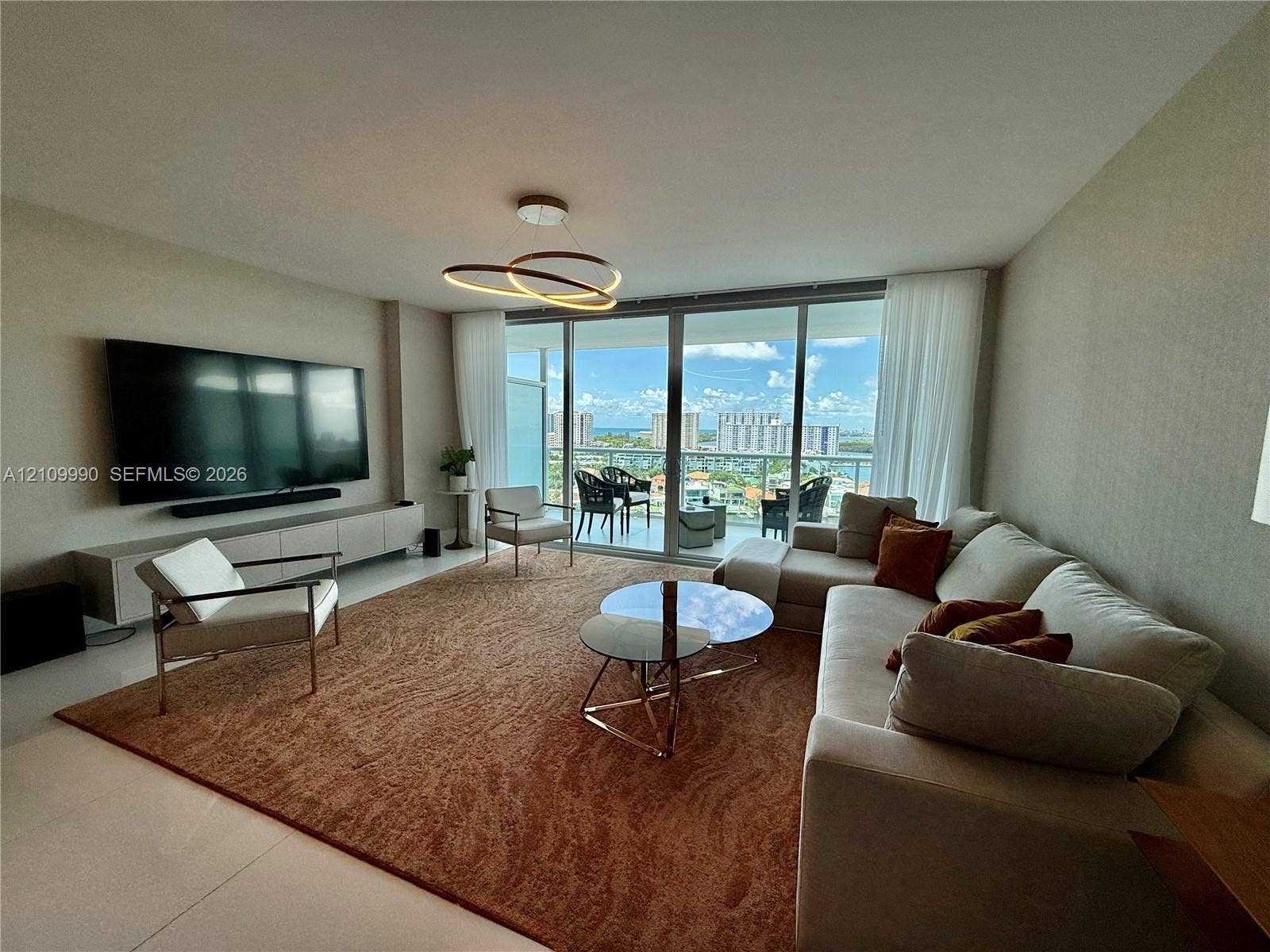 Living area featuring floor-to-ceiling glass sliding doors, built-in wall-mounted cabinetry, polished tile flooring, and a modern circular LED pendant light fixture