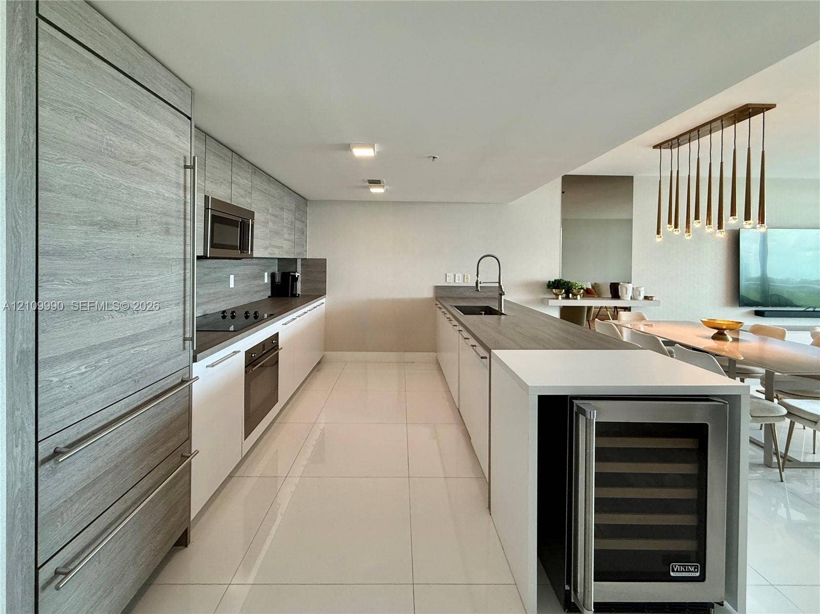 Kitchen featuring flat-panel wood-finish cabinetry, stainless steel built-in refrigerator, integrated wine cooler, stone-surface countertops, and multi-pendant lighting fixture