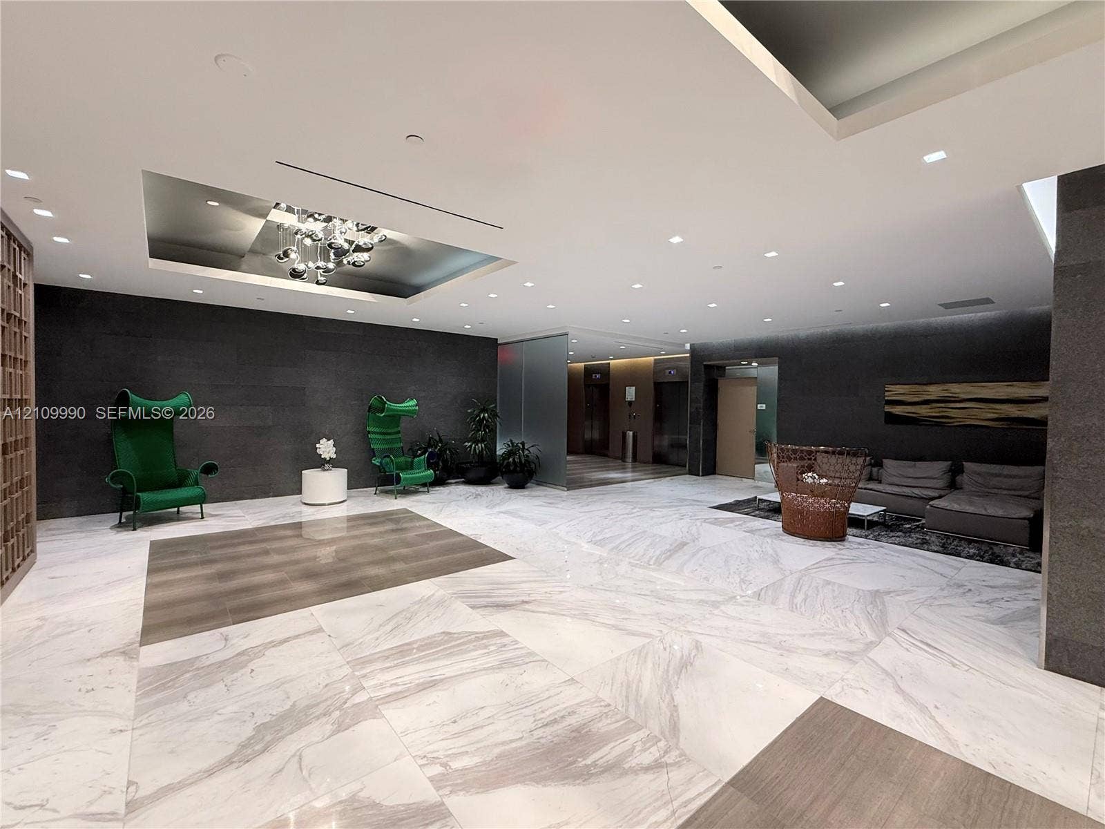 Lobby featuring large-format marble flooring, recessed ceiling lighting with sculptural chandelier, dark stone wall accents, and elevator bank