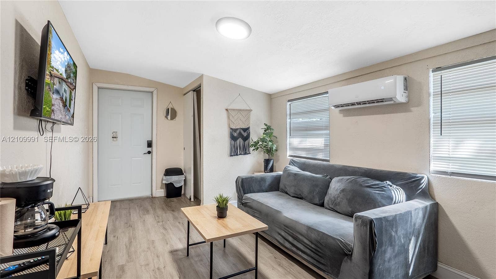 Wood-finish flooring, neutral wall tones, wall-mounted ductless climate control system, and dual windows with horizontal blinds