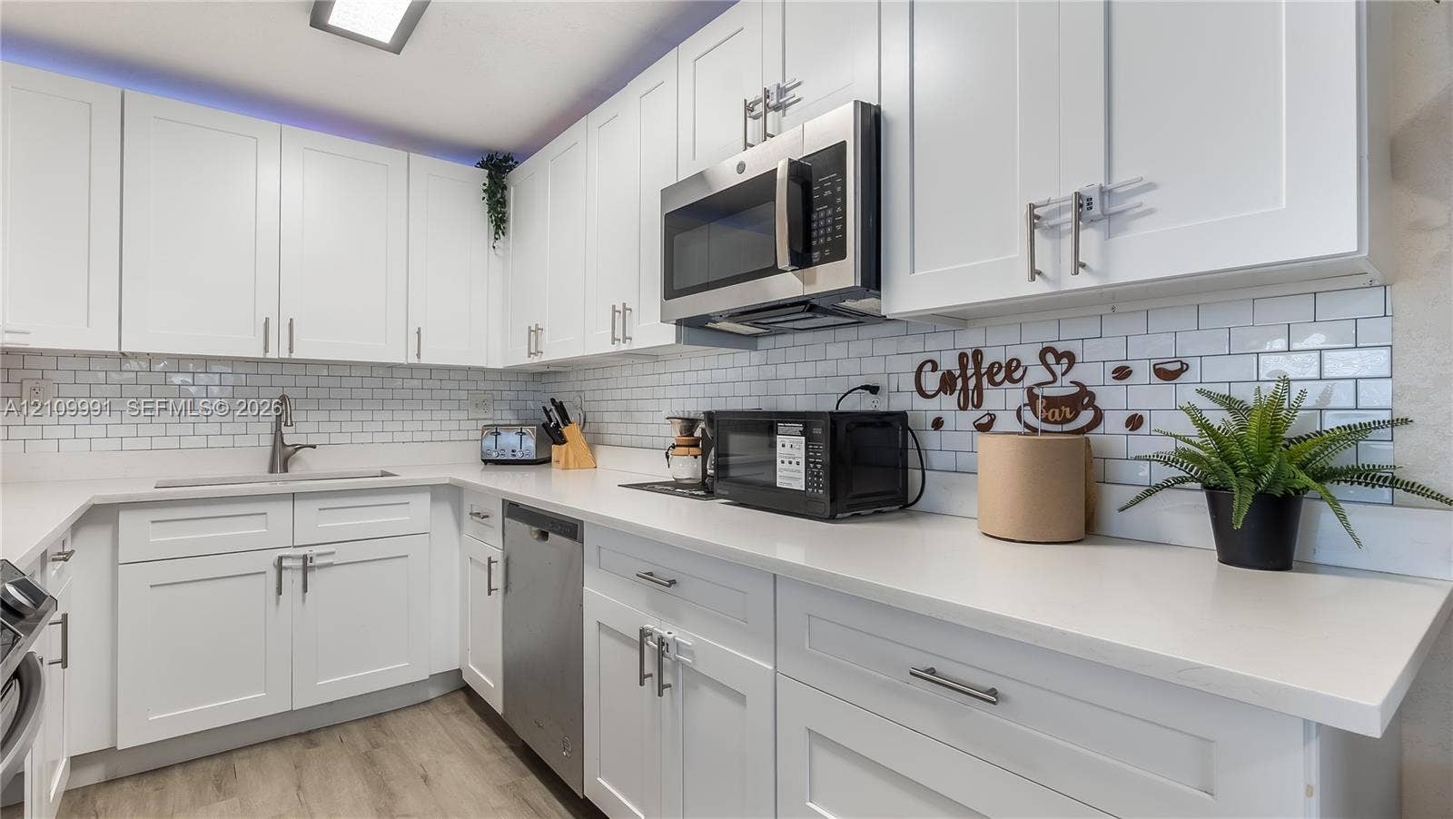 Kitchen featuring white shaker-style cabinetry, solid-surface countertops, a white subway tile backsplash, stainless steel appliances, and wood-finish flooring