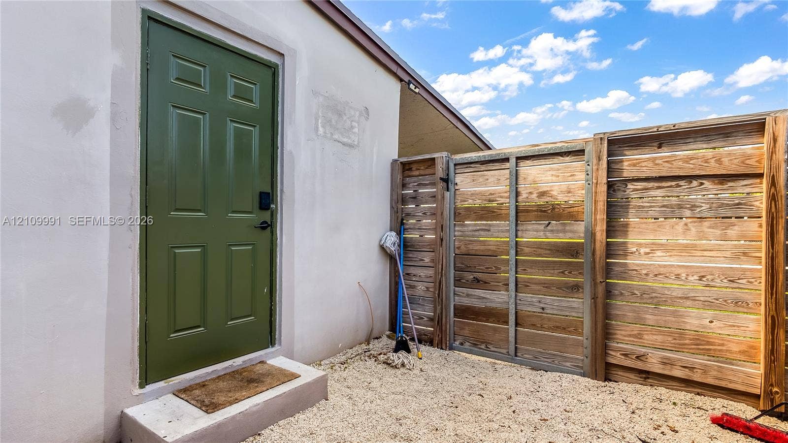 Exterior space featuring a concrete threshold, solid-panel door in olive green, and horizontal-slat wood fencing