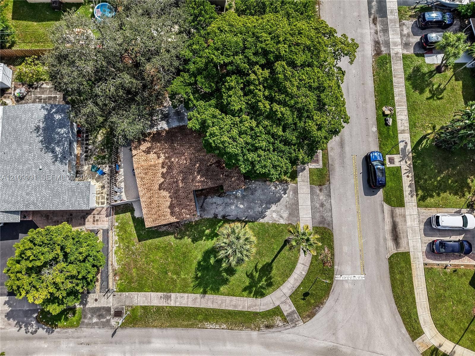 Aerial perspective of corner lot featuring a paved driveway, mature shade trees, and established lawn landscaping