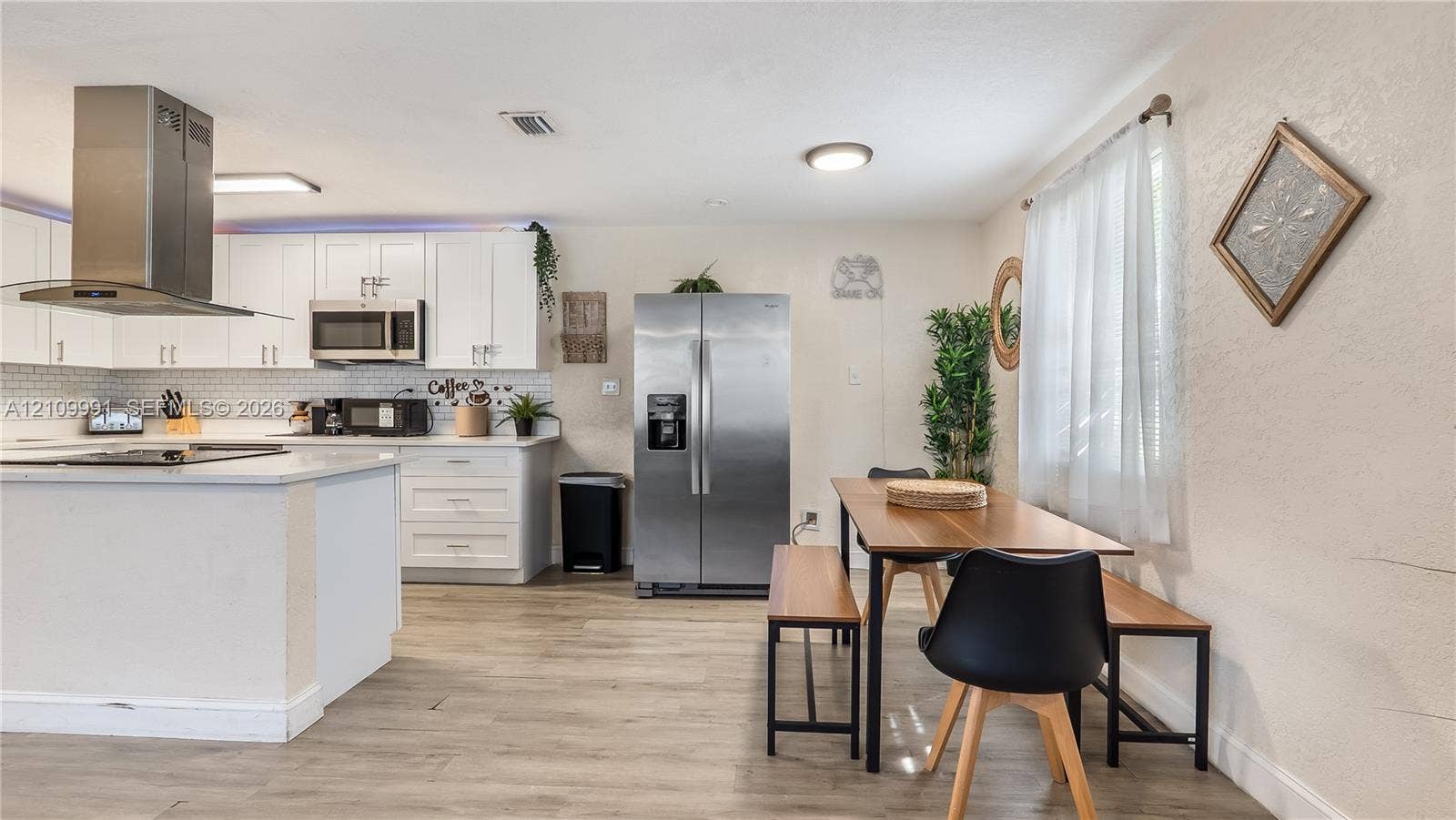 Kitchen featuring white shaker-style cabinetry, quartz countertops, white subway tile backsplash, stainless steel appliances including a chimney-style range hood, and wood-finish flooring