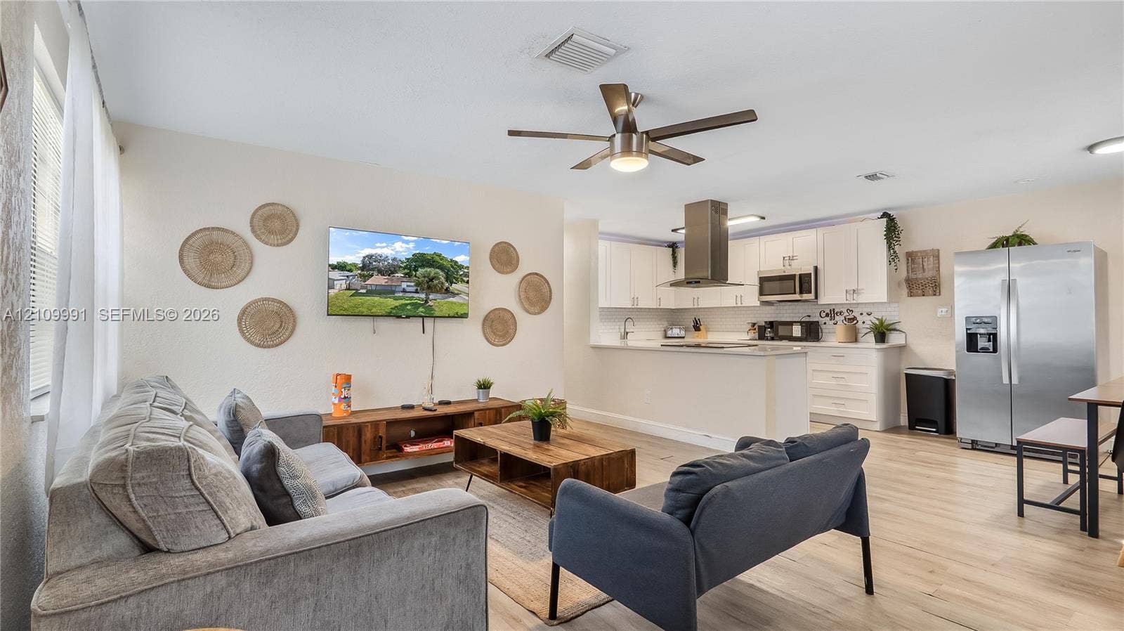 Open-concept interior featuring wood-finish flooring, white cabinetry, stainless steel appliances, a chimney-style range hood, and a ceiling fan