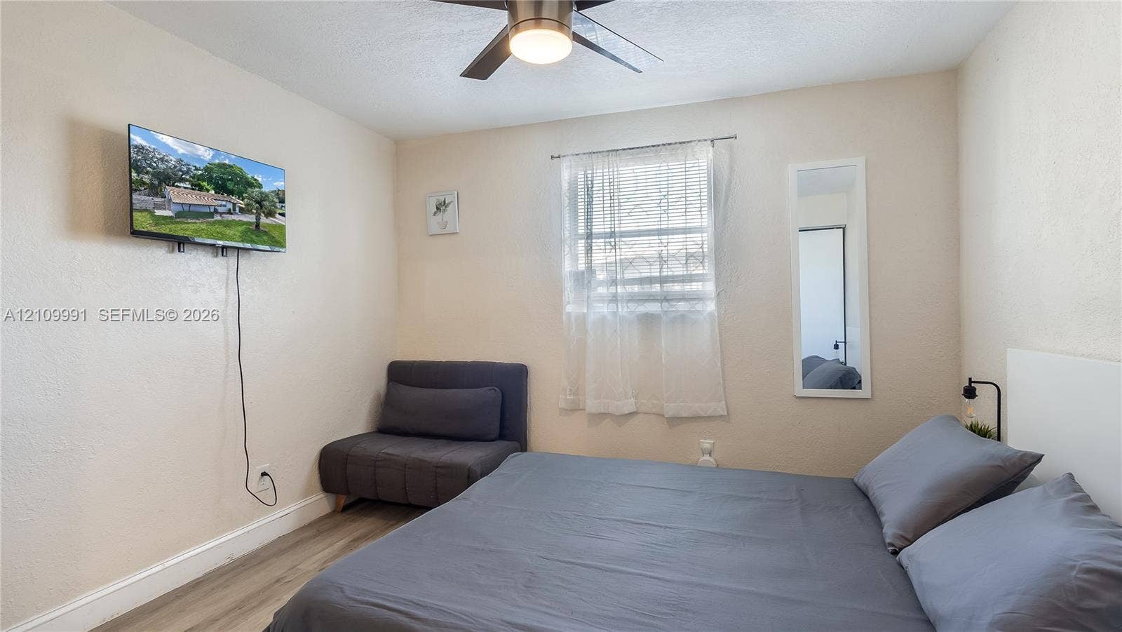 Room featuring wood-finish flooring, a ceiling fan with integrated lighting, and a single window with a horizontal blind
